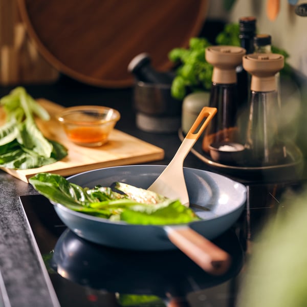 A KNORRHANE spatula stirring leafy greens in a frying pan on a stovetop.