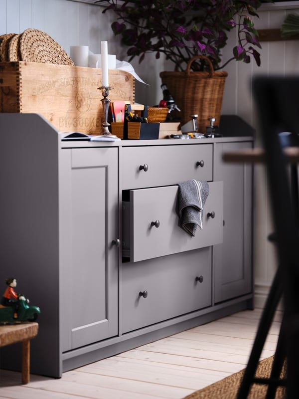 A corner of a wooden-floor dining room with a grey HAUGA sideboard covered in decorations and dining accessories.