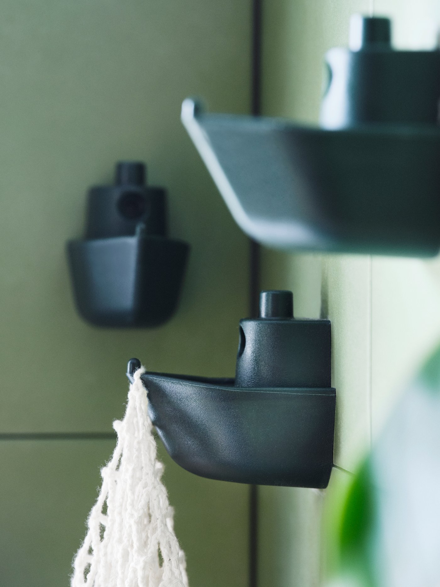 Three green KNOPARE hooks in the shape of the front half of a toy boat mounted at different heights on a green wall.