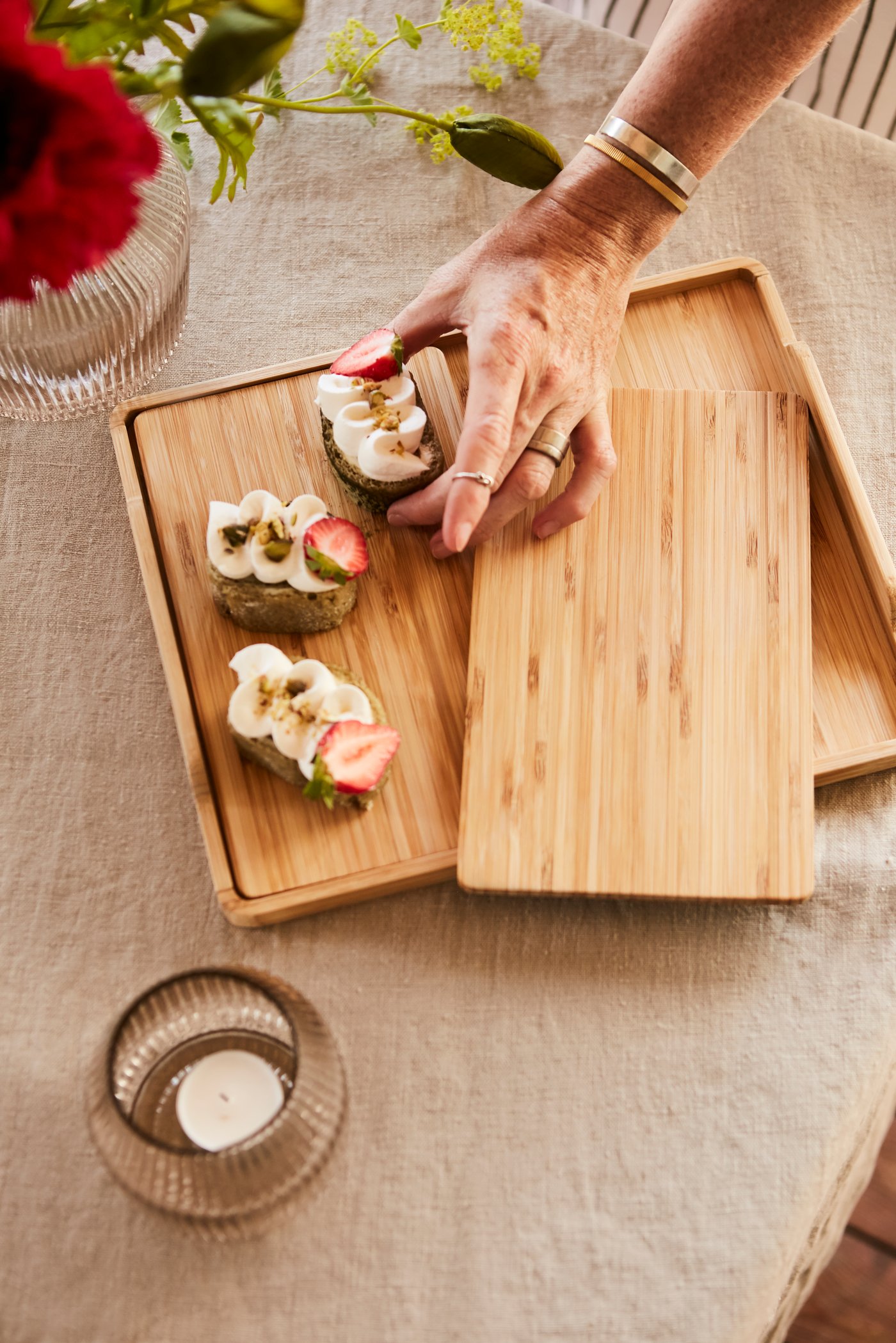 A wooden board used for snacks and treats. A hand can be seen picking up a small bite. 
