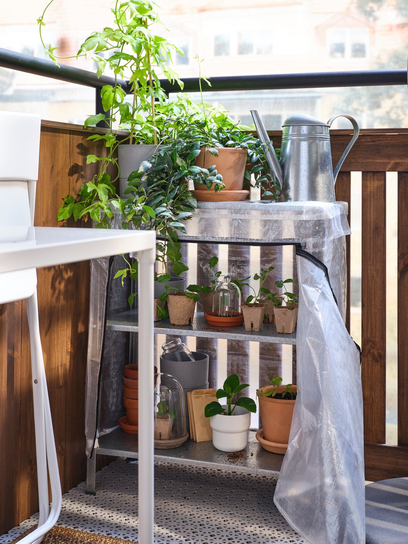 La esquina de un balcón con un estante HYLLIS que tiene plantas en maceteros y artículos de jardinería en sus repisas.