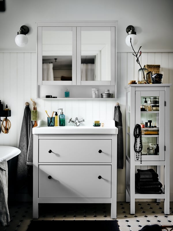 A HEMNES/RÄTTIVIKEN wash-stand with two drawers in a sunny white country-style bathroom with a mirror door cabinet above.