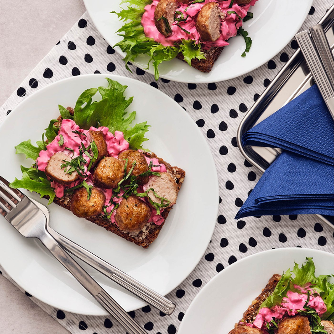 Tartine de pain de seigle garnie de boulettes, salade de betteraves roses et laitue, servie sur des assiettes blanches.