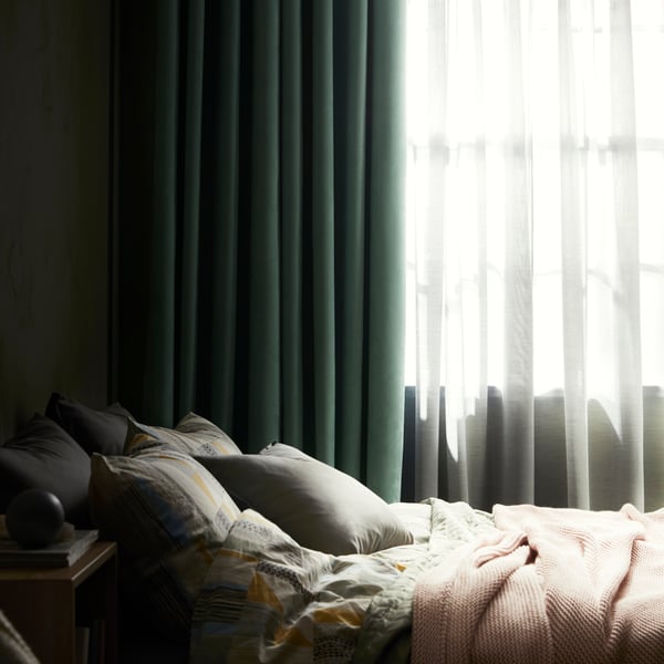 Green curtain blocking light from a bedroom. A bed is seen in the foreground of the image.