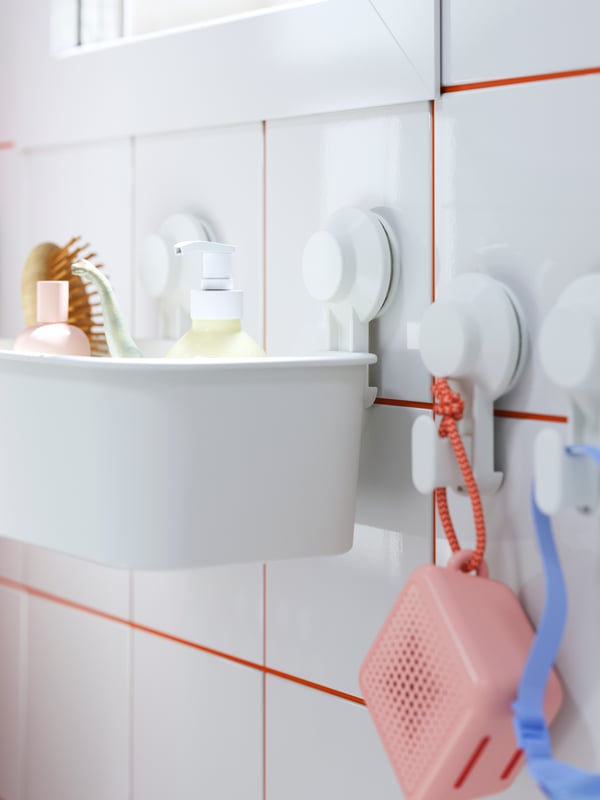 A bathroom with TISKEN hooks with suction cups, holding a pink speaker next to a basket with a soap dispenser and brush.