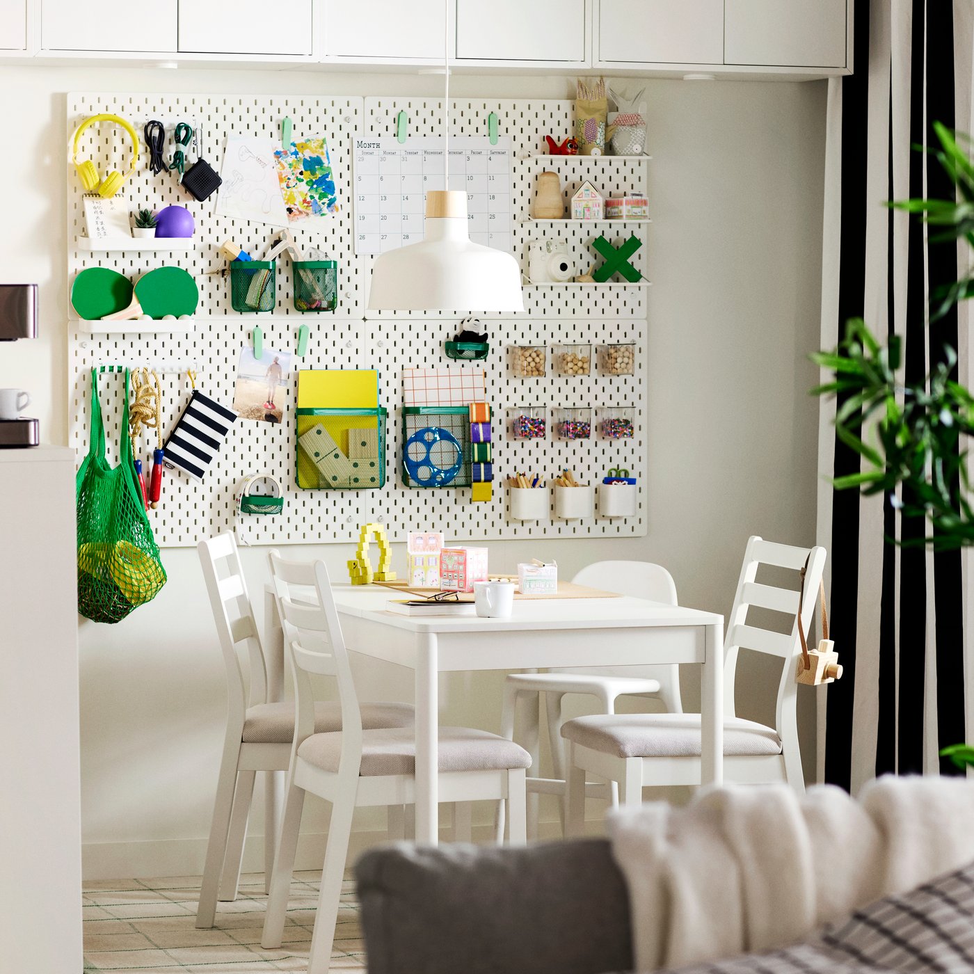 An off-white TONSTAD extendable table surrounded by four white chairs, set in a bright dining area with wall-mounted storage.