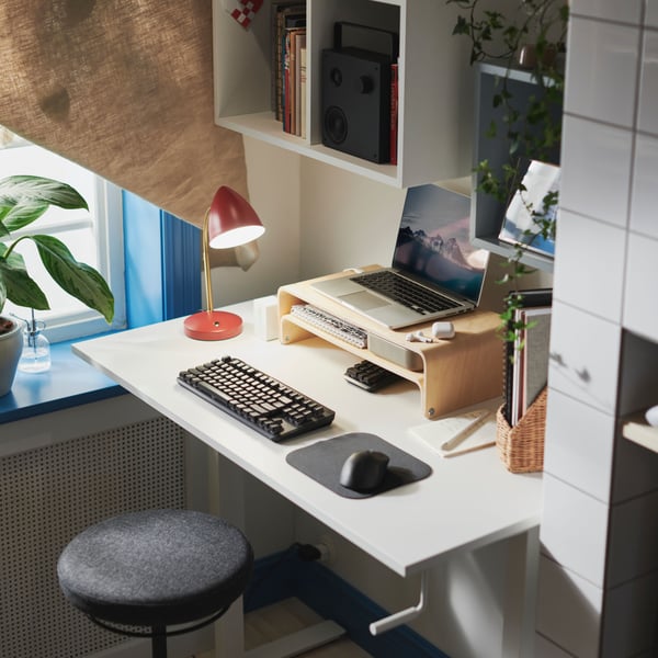 Es ist ein Arbeitsplatz mit einem TROTTEN Sitz-/Stehschreibtisch und einem VATTENKAR Laptop-/Monitorständer zu sehen, auf dem ein Laptop liegt.
