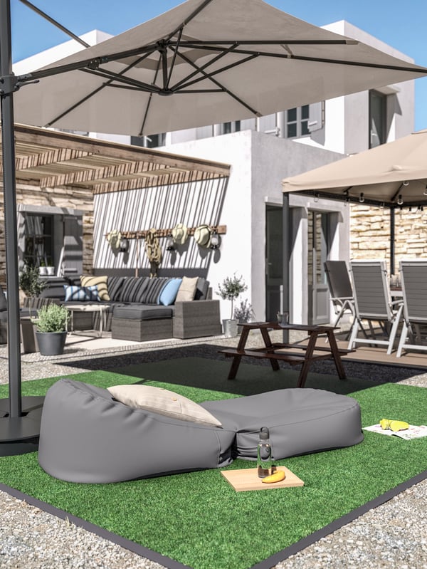 Green artificial grass decking, a grey bean bag with a cushion, a children's picnic table and a large beige parasol.