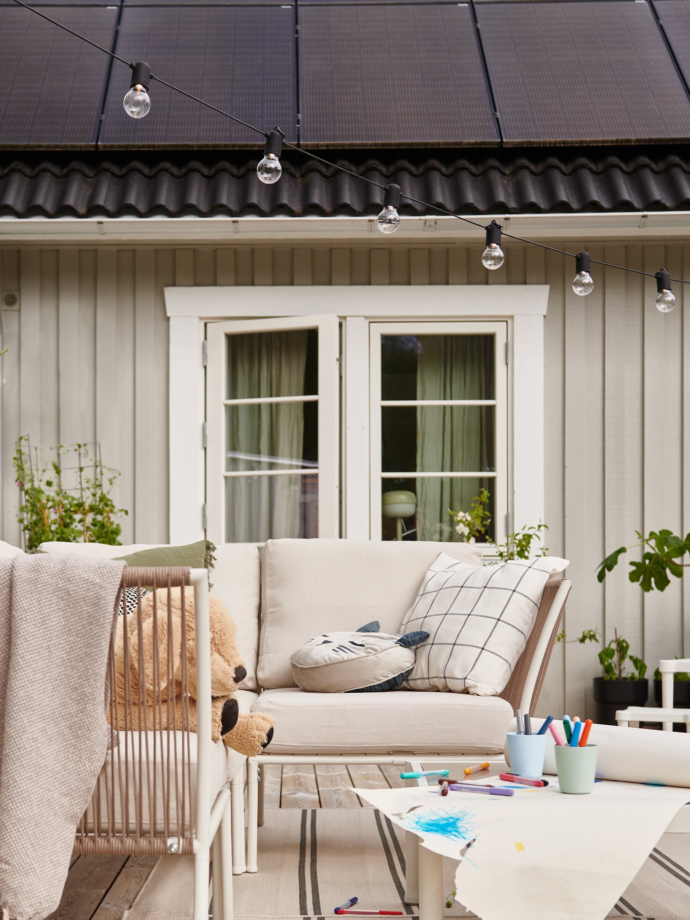 Ett hus med solceller på taket och på uteplatsen står ljusa utemöbler.