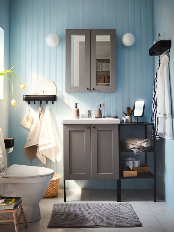 A bathroom with blue walls, ENHET bathroom furniture, a grey mat, a LILLASJÖN wall shelf with 5 hooks and white wall lamps.