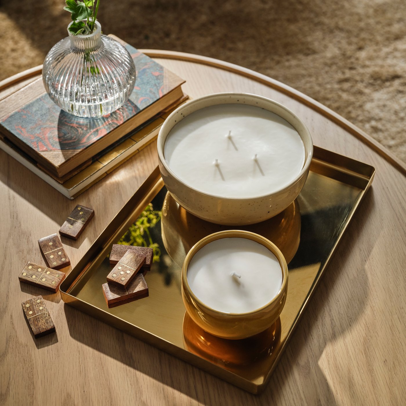 Two PÄRLHÖNA scented candles sit on a gold tray in a living room with wooden dominoes and a glass vase.