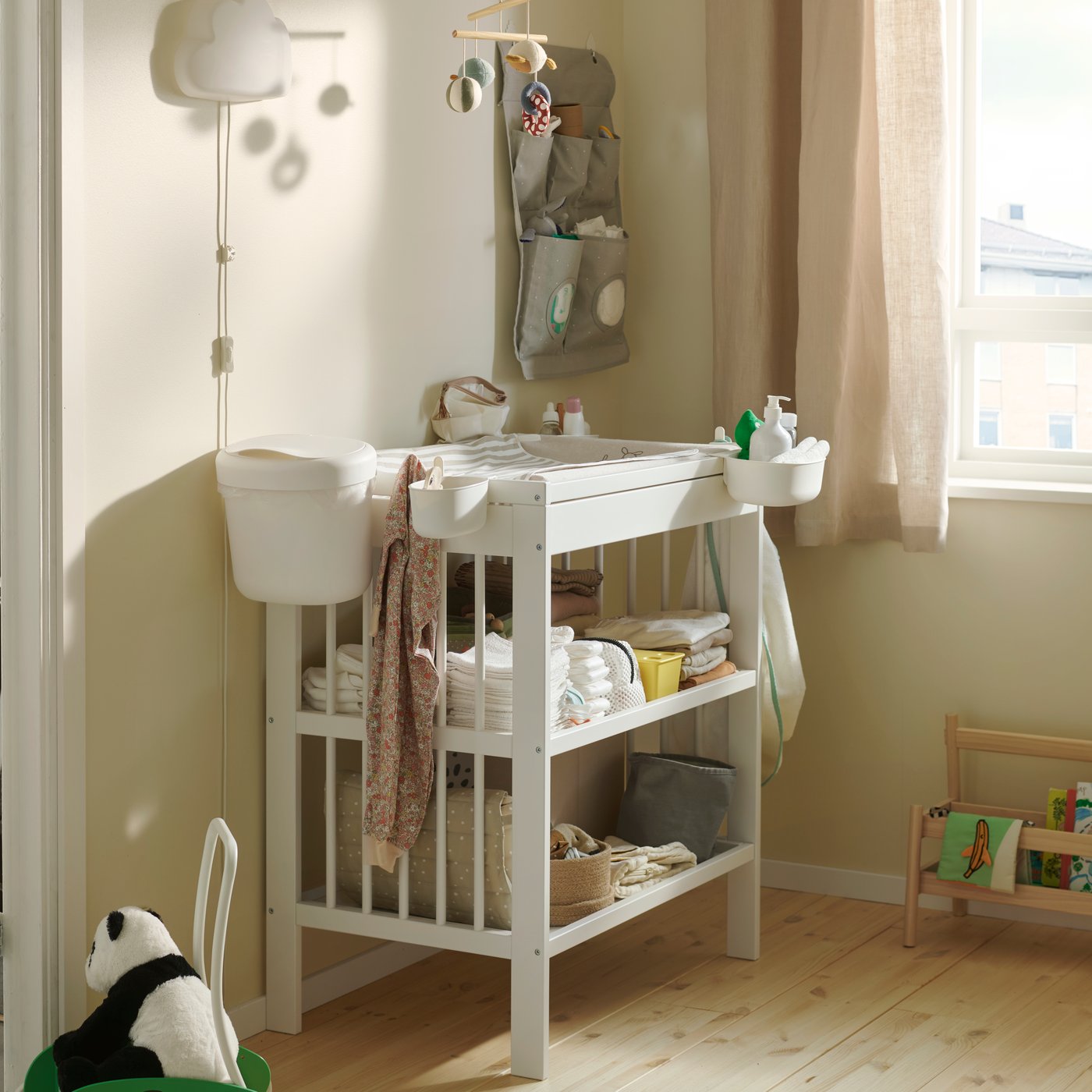 A nursery with beige walls and a GULLIVER changing table, its shelves stocked with nappies and baby items.