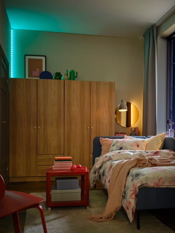 A multicolour VATTENSTEN LED light strip showing green placed vertically above a wardrobe in the corner of a dark bedroom.