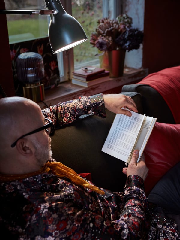 In einem kuschelig eingerichteten Zimmer liest eine ältere Person in einem Buch, unterstützt durch eine ARÖD Stand-/Leseleuchte.