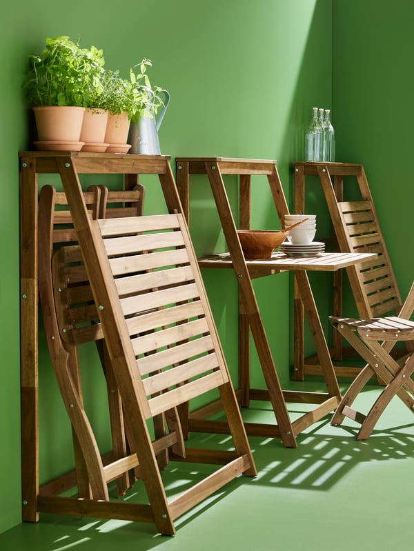 Three DJUPÖN folding tables arranged against a bright green wall. One is folded out and has plates and bowls on top of it.