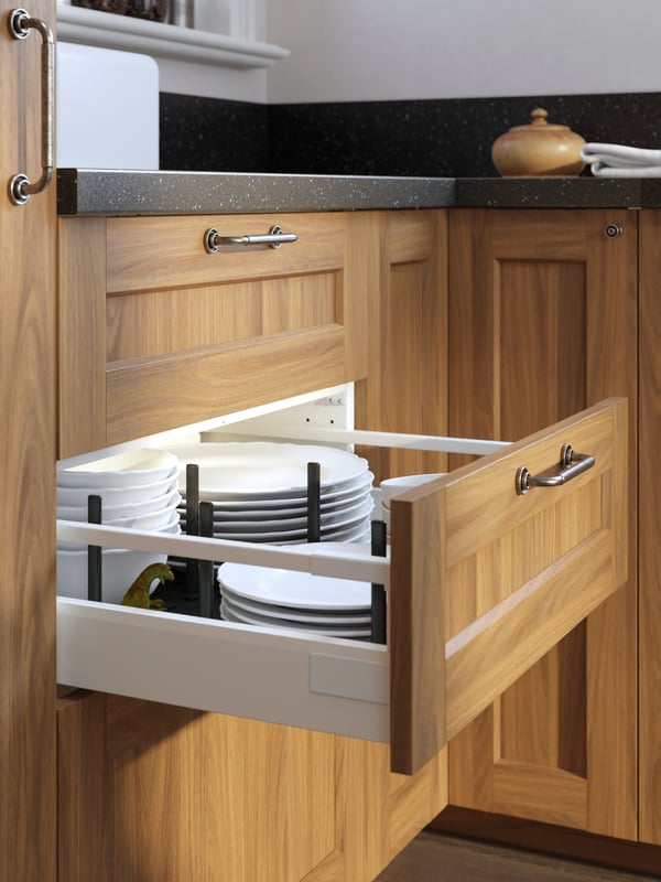 An open kitchen drawer with a brown walnut-effect ENKÖPING front and SKRUVSHULT handle with piles of plates and bowls inside.