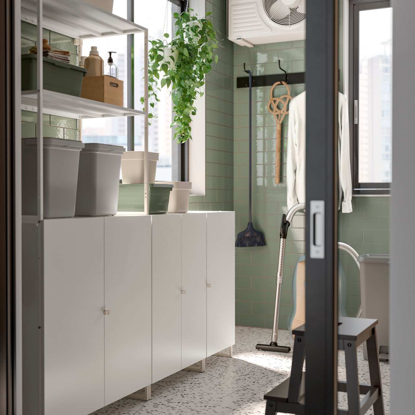 Een lichte, moderne JOSTEIN berging toont open rekken met opbergdozen, een hangende plant en schoonmaakaccessoires naast een raam.