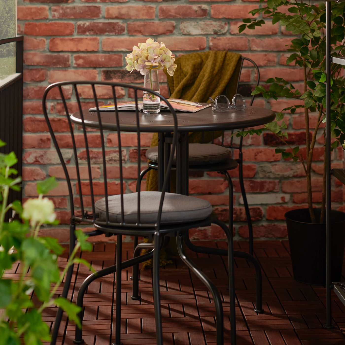 A round steel LÄCKÖ outdoor table with two black steel LÄCKÖ outdoor chairs on a balcony with wooden RUNNEN decking.