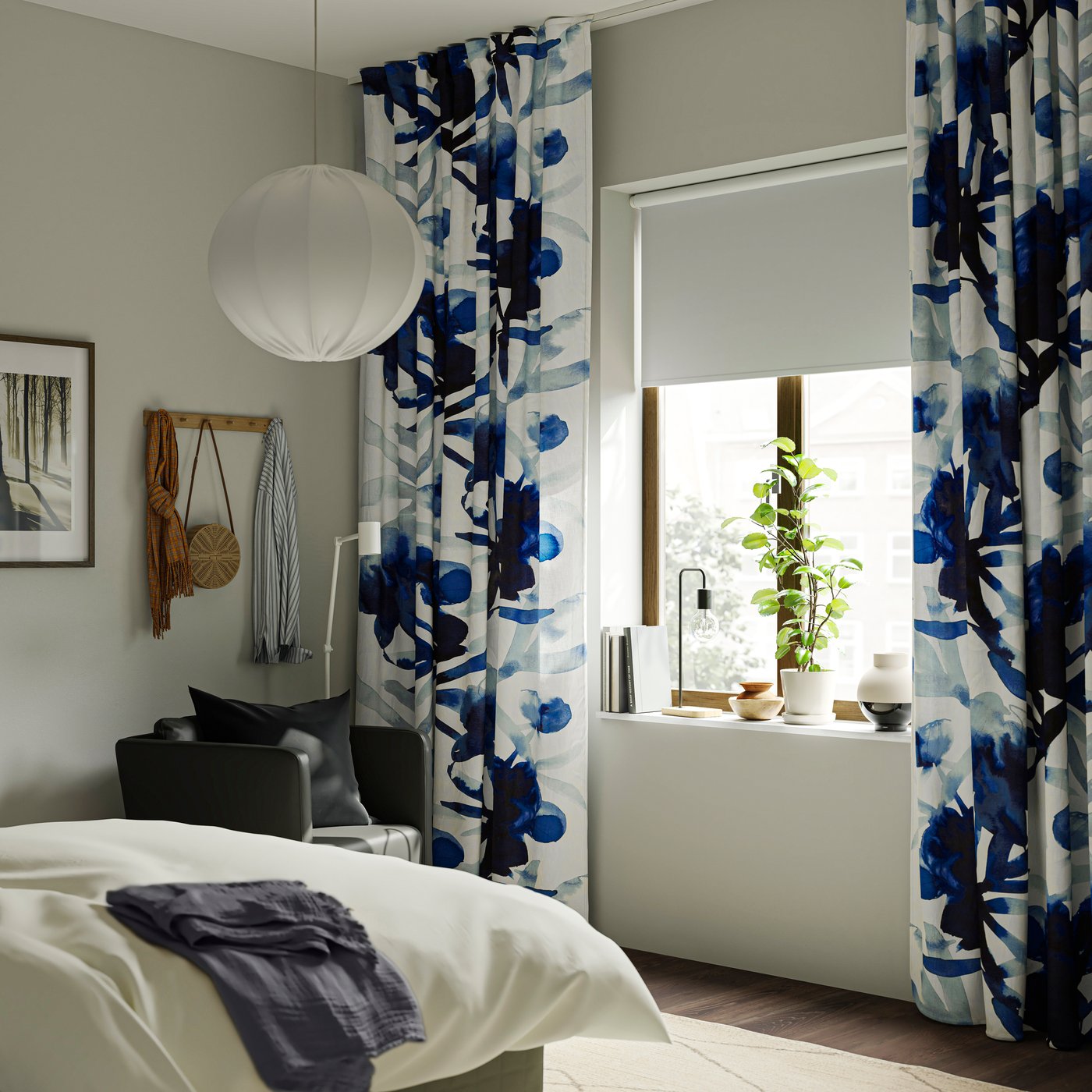 A bedroom with white/blue SKOGSNÄSSLA curtains adorned with a floral pattern.