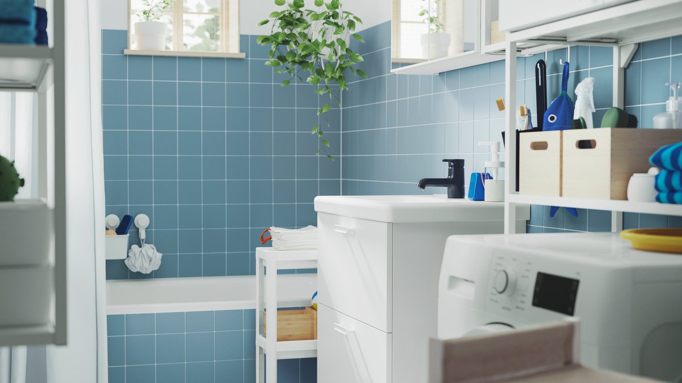 A blue-tiled bathroom with a bathtub has a white ENHET base cabinet, a wall cabinet with mirror doors and a VESKEN trolley.