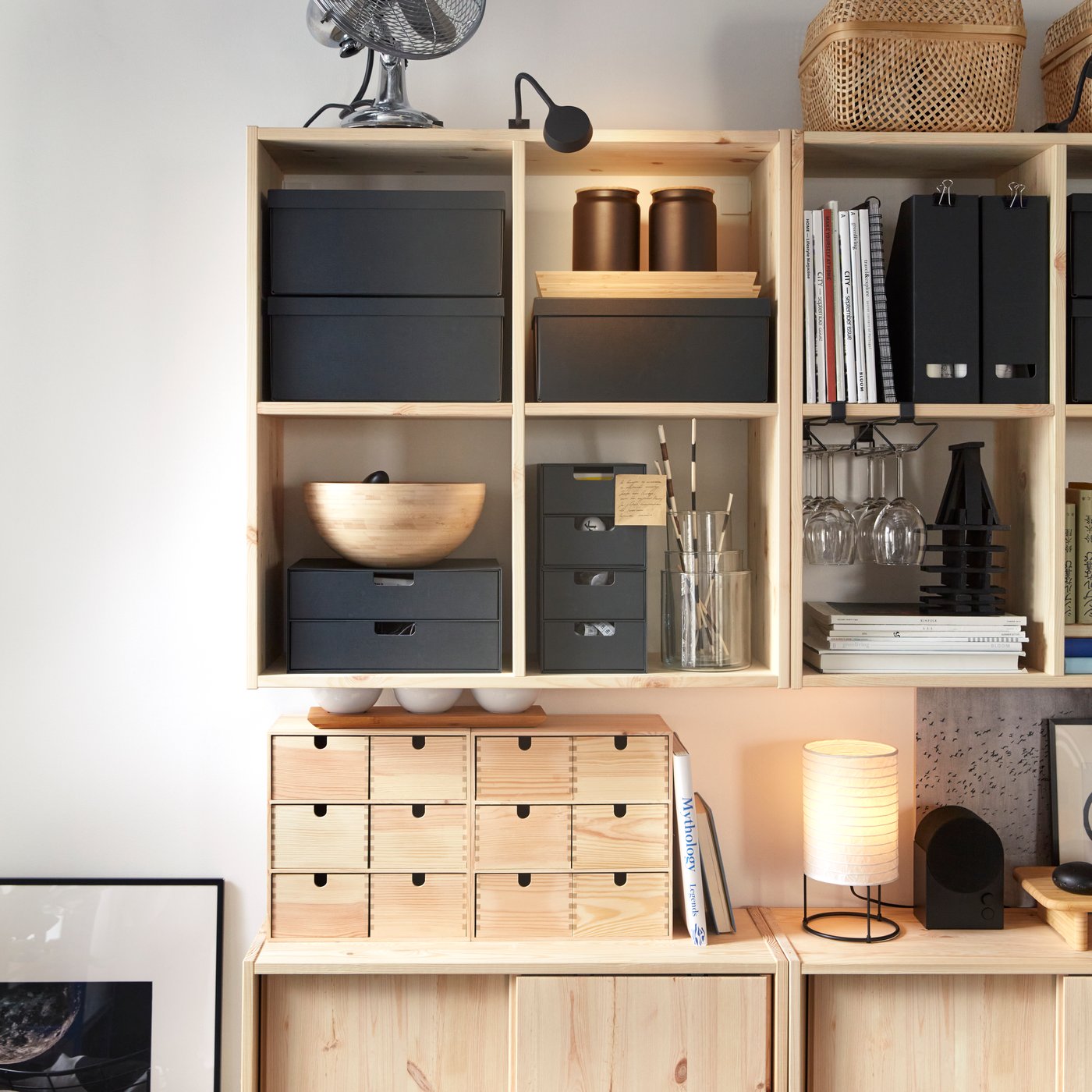 Two IVAR wall shelves in pine holding black storage boxes and other objects, placed above IVAR cabinets with sliding doors.