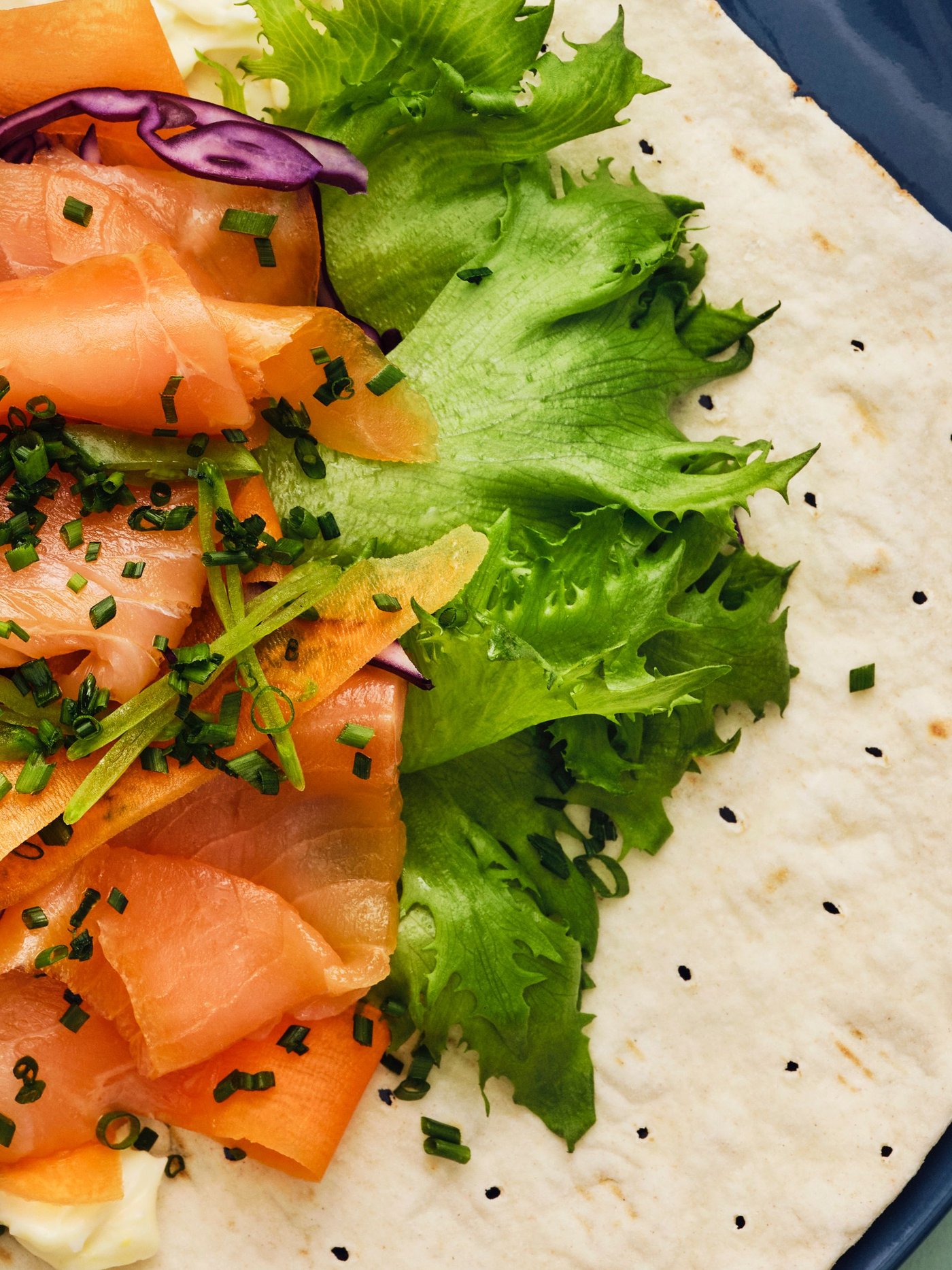GRÄDDAT soft thin flatbread topped with SJÖRAPPORT cold-smoked salmon, lettuce, and purple cabbage, served on a blue plate.