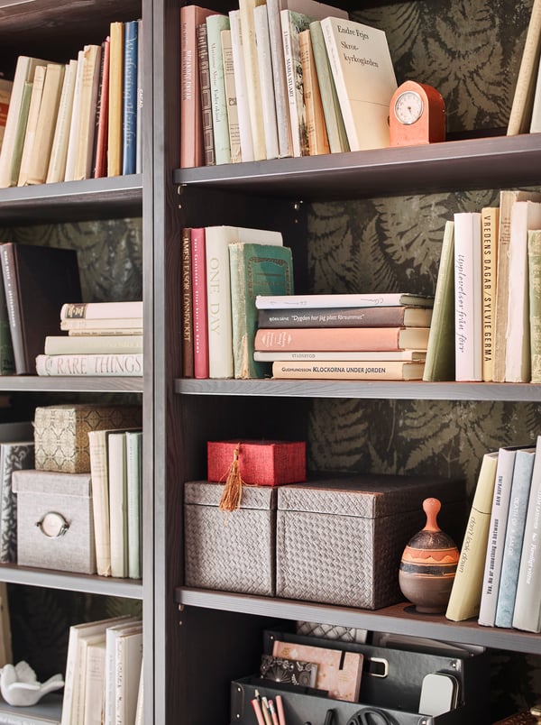 A grey HAVSTA storage combination is filled with decorative items, books, rattan baskets, vases and dried flowers.