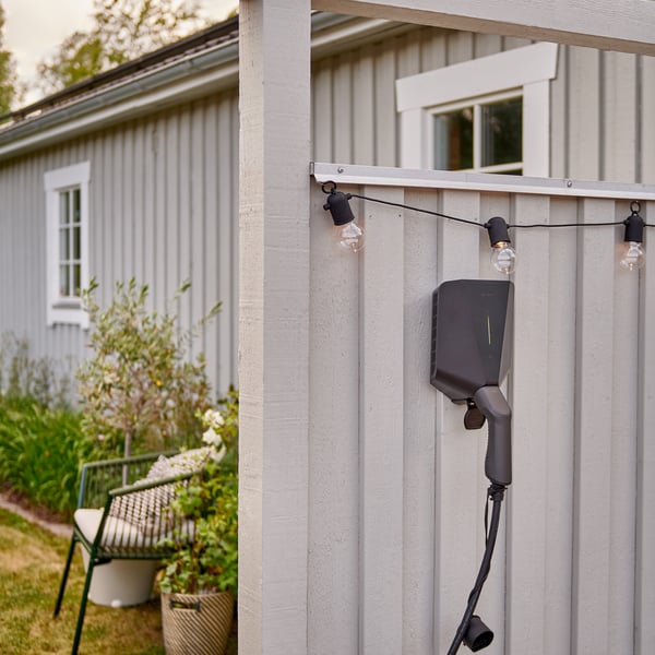 Une station de recharge pour véhicules électriques installée à l’extérieur d’une maison, sur un revêtement gris clair.
