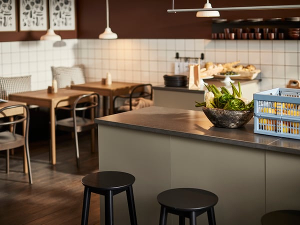 Une salle à manger chaleureusement aménagée présente des tables et chaises en bois, un comptoir avec des tabourets et un panier de plantes.