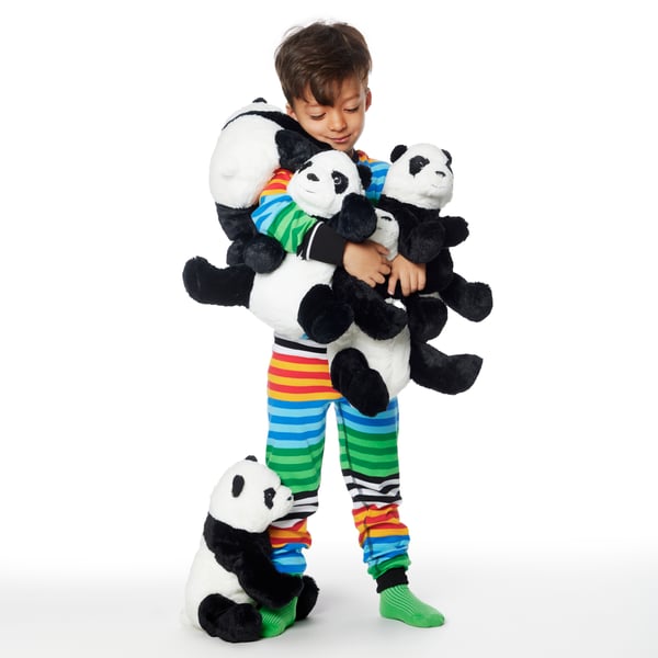 A child in colourful striped pyjamas stands cuddling several KRAMIG soft toy panda bears.