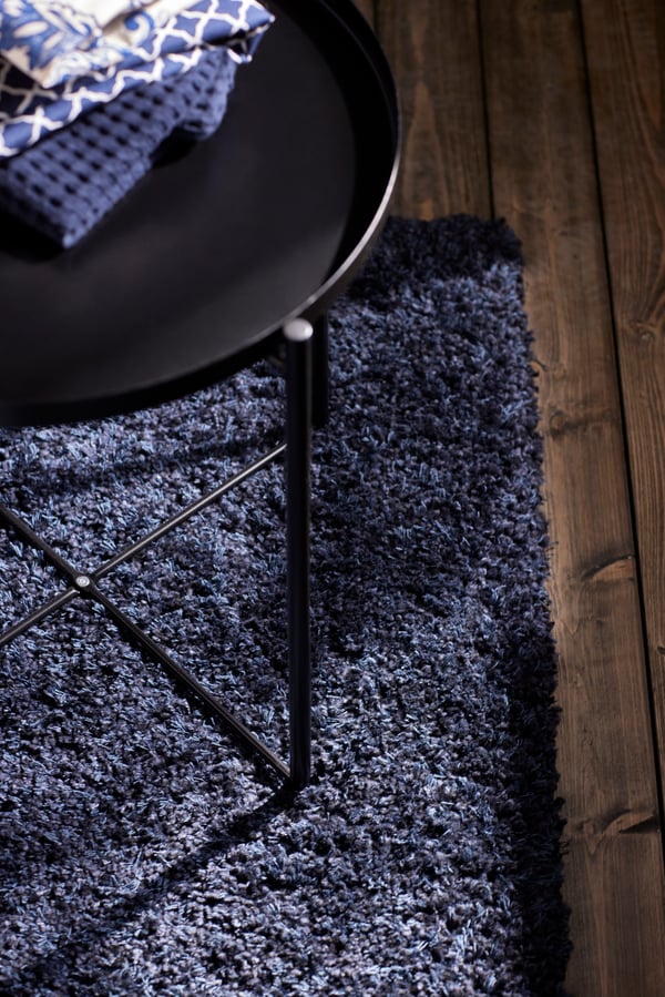 Vue d’un canapé en velours bleu foncé sur une fenêtre avec de longs rideaux blancs transparents et des rideaux occultants, ainsi qu’une table basse en verre et une plante.