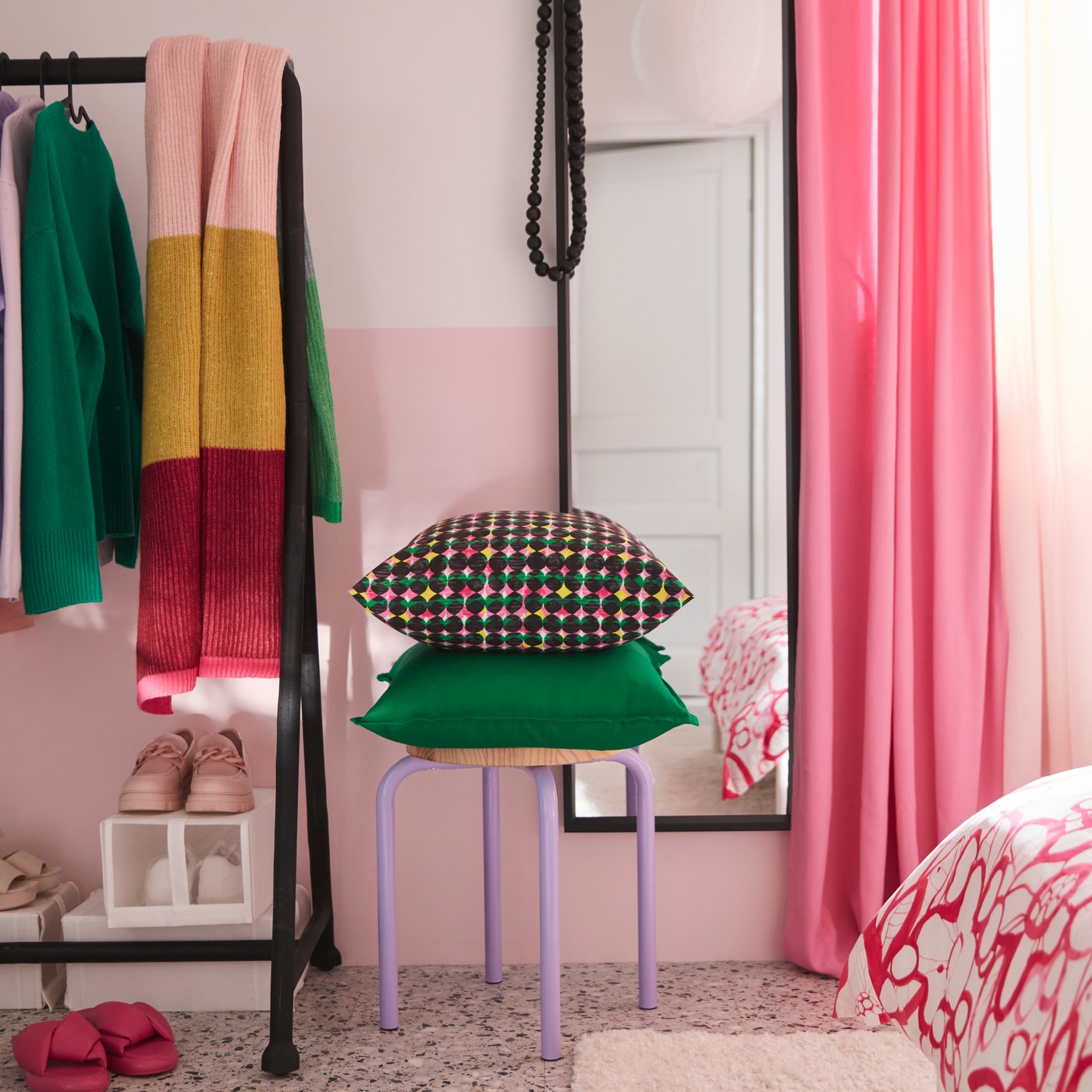 Chambre avec tabouret où sont empilés un coussin revêtu d’une housse de coussin ÄLVSJÖSKOGEN rose/vert et un coussin revêtu d’une housse de coussin GURLI verte.