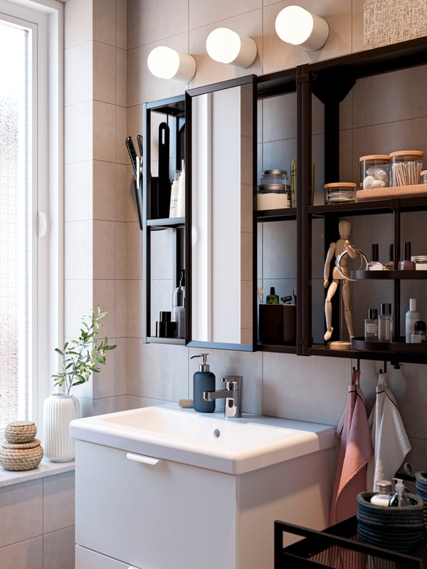 A black wall frame with shelves, sliding mirror and swivel tray, a white wash-stand/wash-basin and three white wall lamps.