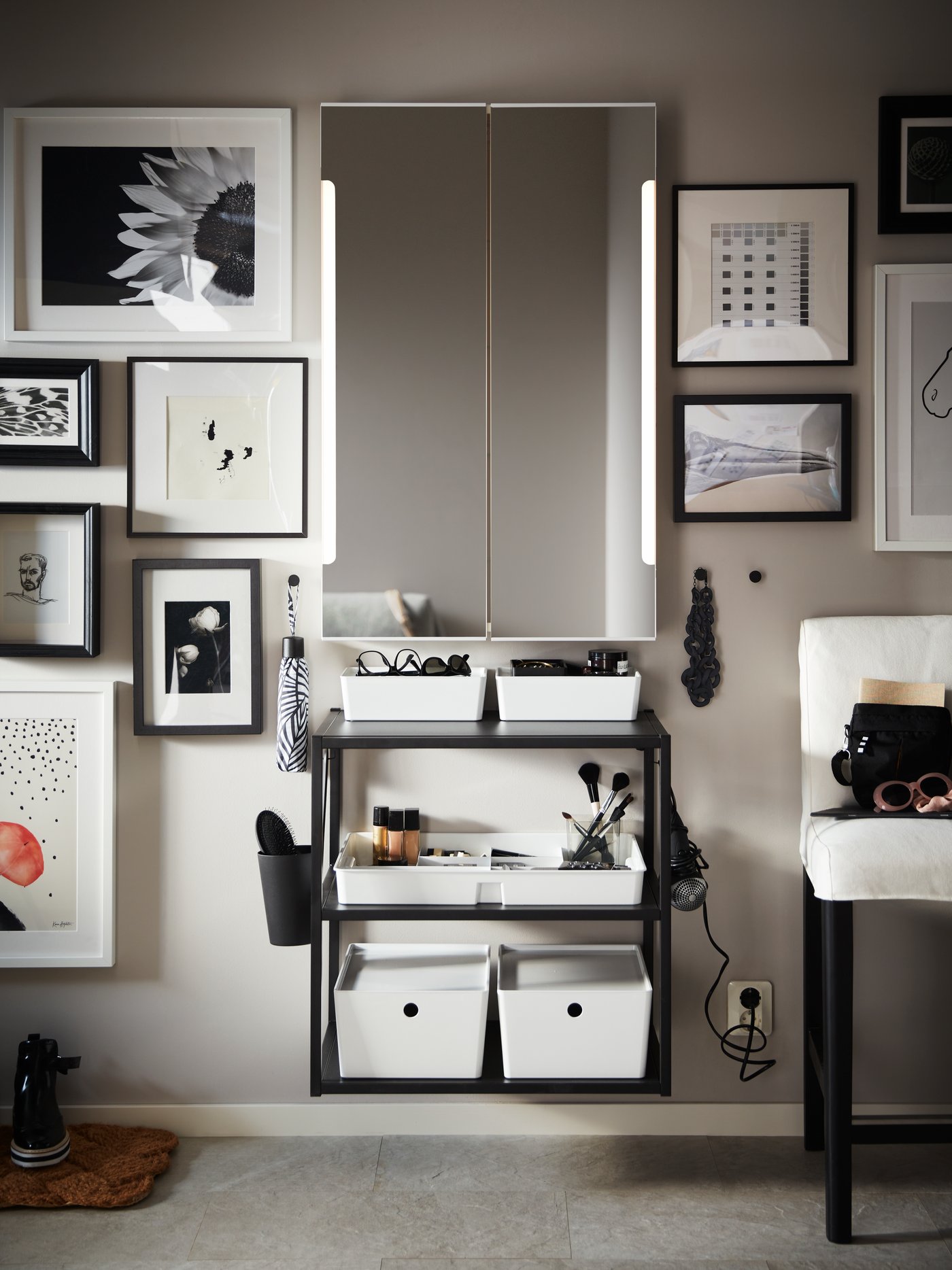 A white STORJORM mirror cabinet with built-in lighting on a wall with framed pictures and an anthracite shelving unit.