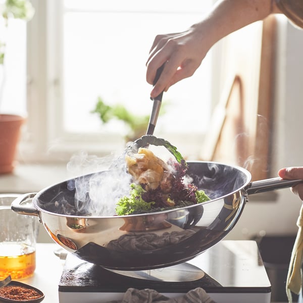 IKEA 365+ frying wok with handle stirfrying a vegetable dish on top of a TILLREDA induction cooker next to a VARDAGEN measuring jug. 
