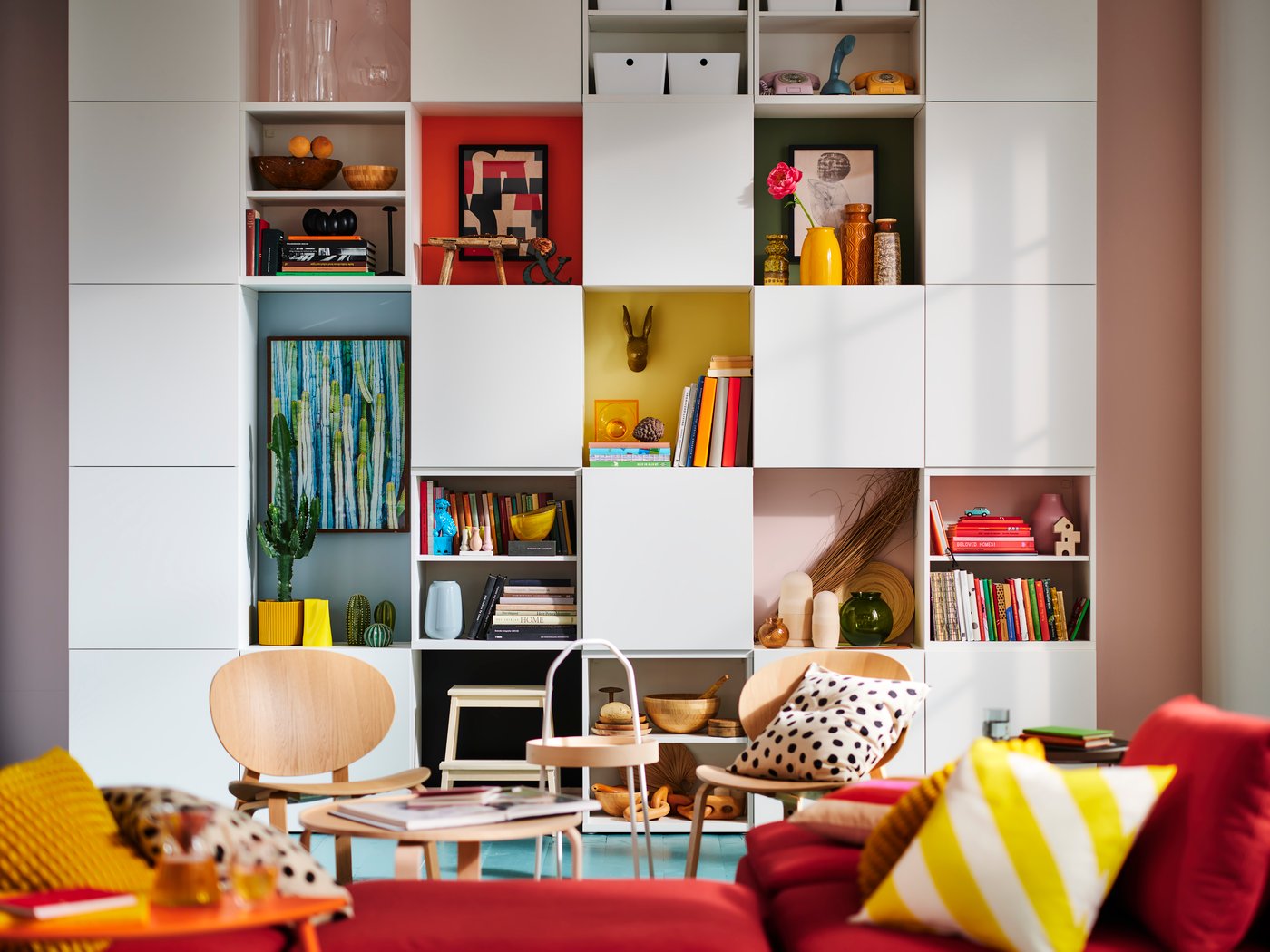A living room with red sofas, pink walls and a white shelving system on the wall.