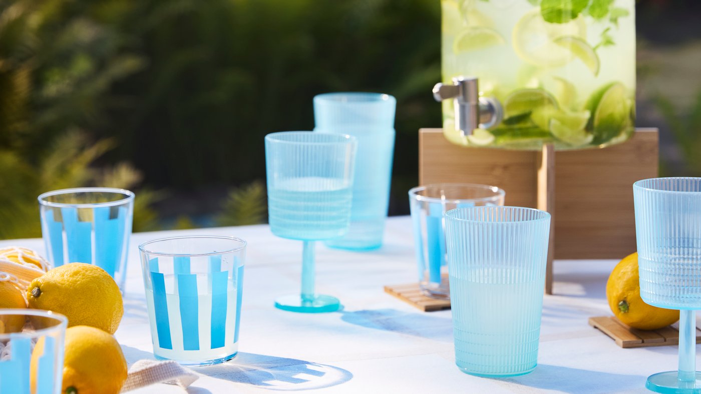 Sur une table d’extérieur, verres KALLSINNIG et PILLESTARR bleus, et fontaine à boisson IKEA 365+ remplie de limonade.