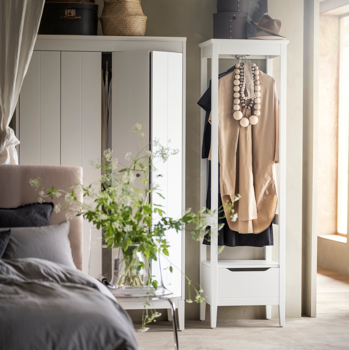 White IDANÄS open wardrobe and a white IDANÄS wardrobe with bifolding doors are on a wall behind an upholstered bed.
