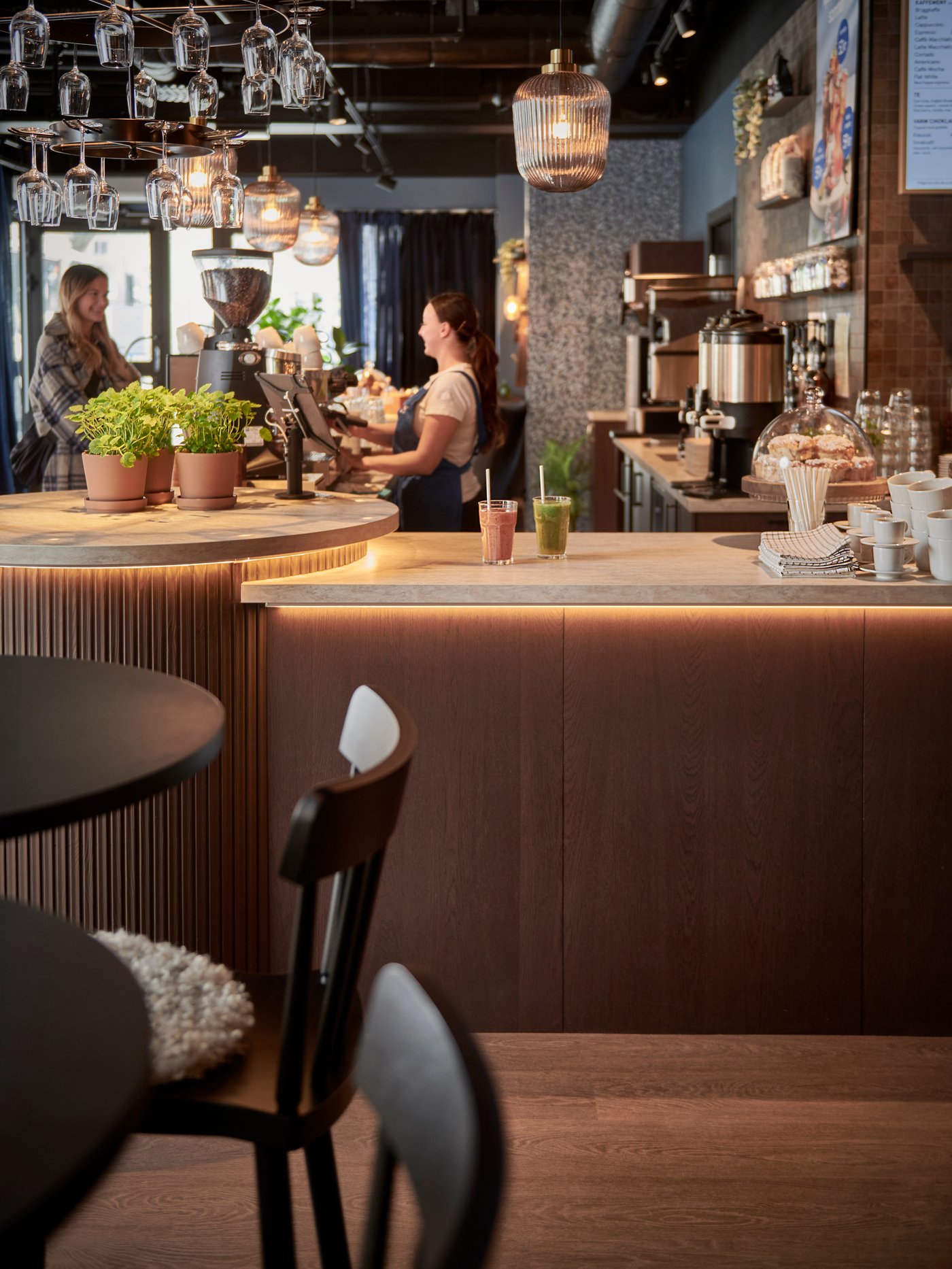 Varmt och inbjudande kafé med träinredning, disk, hängande glas och personal bakom kassan.