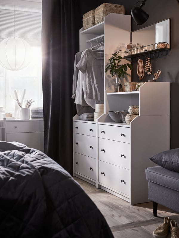 A HAUGA storage combination stands against a wall in a bedroom between a window and a STRANDMON footstool.