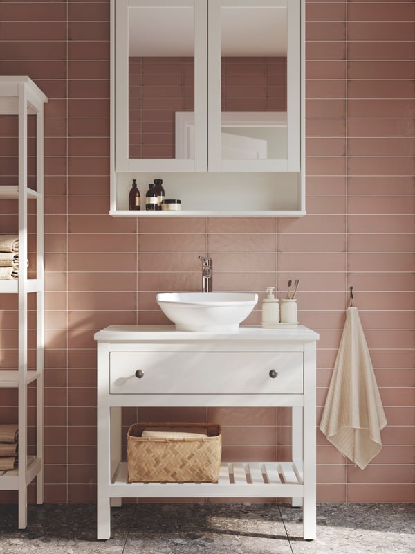 חדר אמבטיה שבו ארון כיור פתוח HEMNES בצבע לבן עם מגירה אחת, כיור מונח VÄSTERSJÖN לבן וארון מראה.