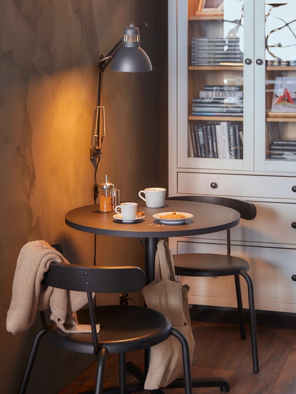 STENSELE café table with chairs, two white coffee mugs on the table, and behind it a white bookcase with glass doors.