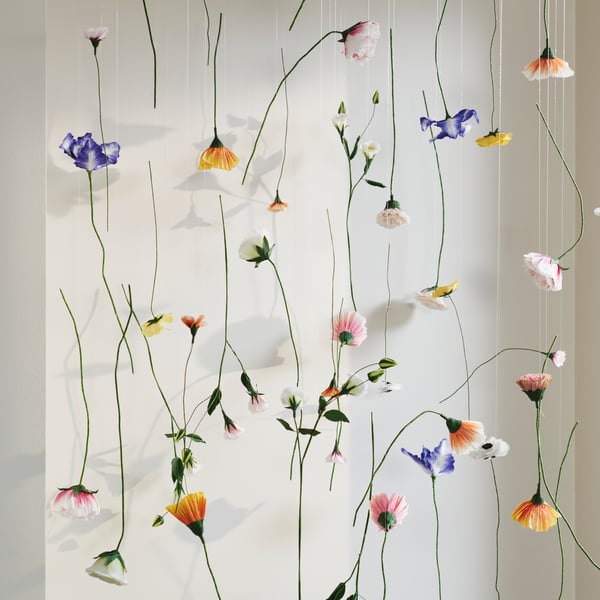 A lot of GULDSPETT artificial flowers are hung on different pieces of string to form a decoration in front of a wall.