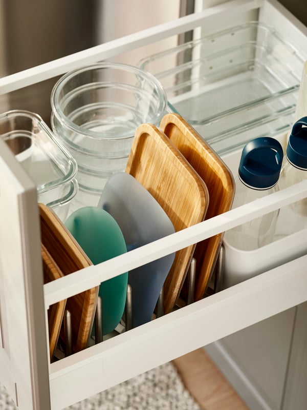Un cajón de cocina con contenedores de alimentos de vidrio IKEA 365+ ordenados por tamaño. Las tapas, correspondientes a cada pocillo, están ordenadas a un costado y los recipientes al otro.