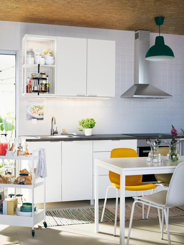 A light kitchen with ENHET cabinets, a white MELLTORP table, different-colour LEIFARNE chairs and a white NISSAFORS trolley.