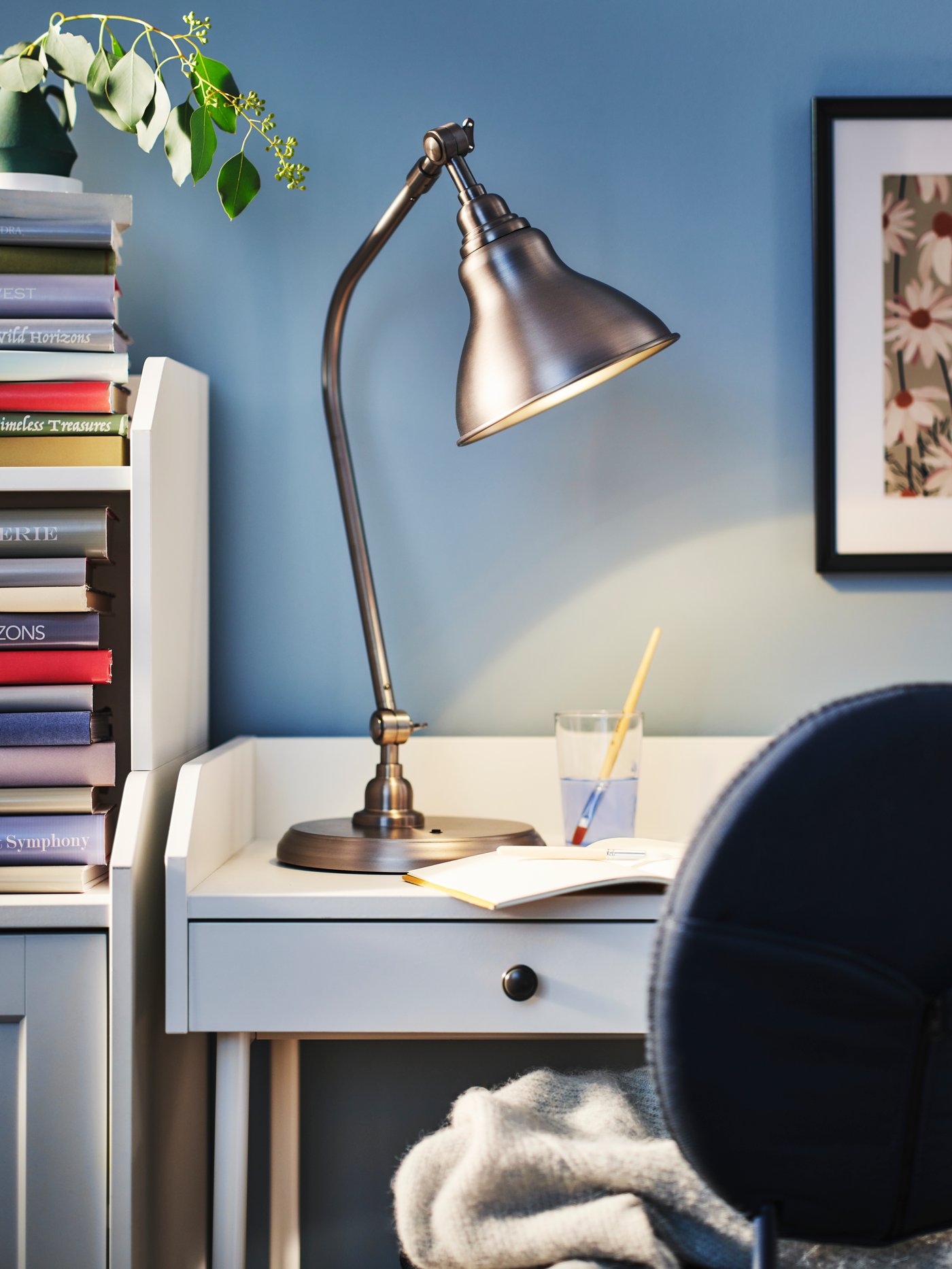 A pewter effect ANKARSPEL work lamp stands on a white HAUGA desk standing next to a blue BJÖRKBERGET swivel chair.