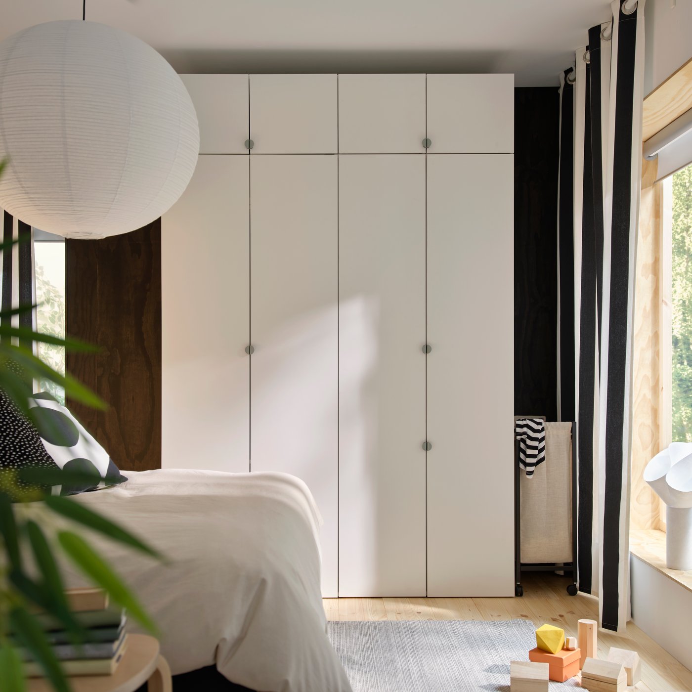 LASTARE wardrobe combination in white with tall doors and upper cabinets placed along the wall in a modern bedroom.