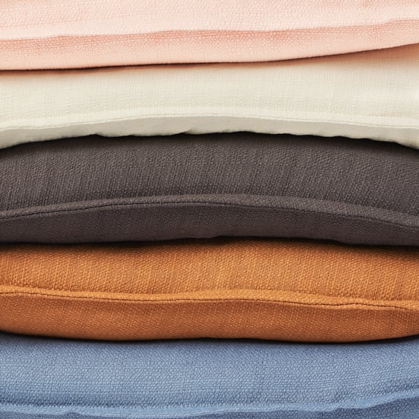 Close up on a stack of different coloured LAGGERPOPPEL cushion covers, showing the side seams and fabric texture.