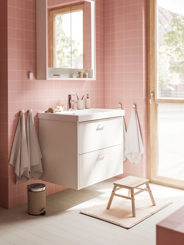 A white HAVBÄCK vanity with drawers and a mirror cabinet are placed in a bathroom with soft pink walls and a grey floor.