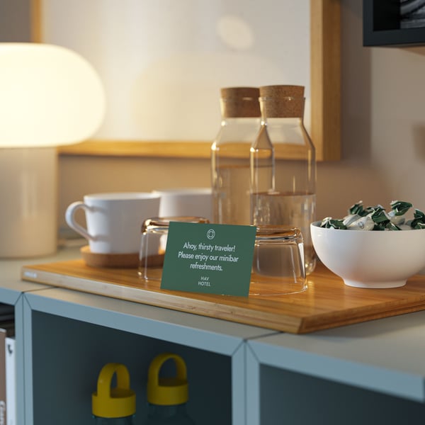 Auf EKET Schränken ist eine kleine Bar mit IKEA 365+ Karaffen aus Glas, weissen Bechern, Gläsern und einer Schüssel mit Süssigkeiten auf einem Schneidebrett zu sehen.